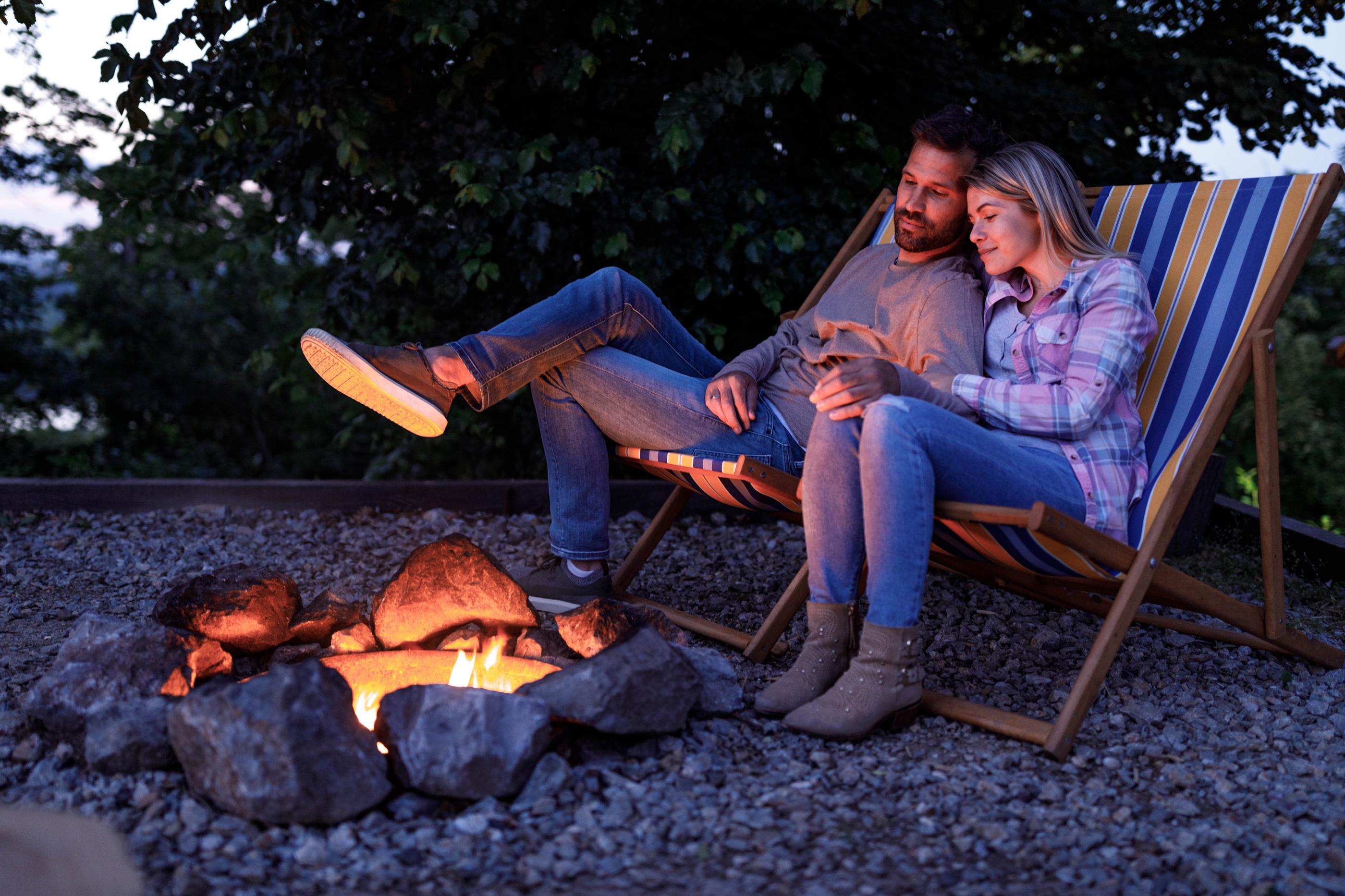 A person and person sitting in chairs by a fireDescription automatically generated