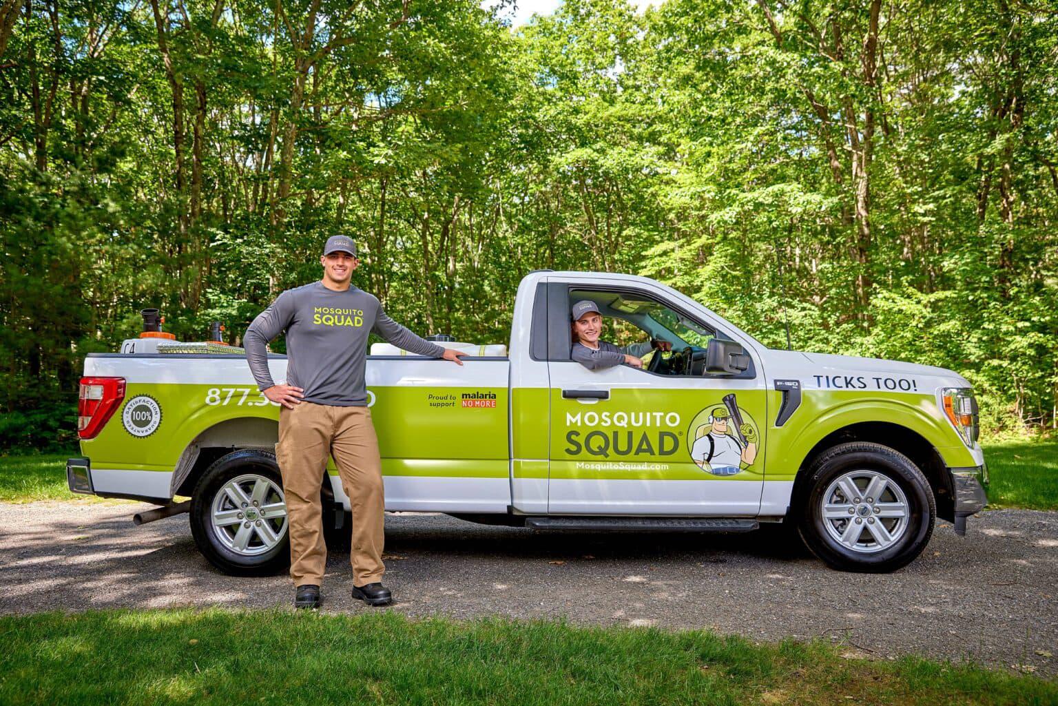 Mosquito Squad truck with bold branding for mosquito and tick control, parked outdoors with two team members ready for service.