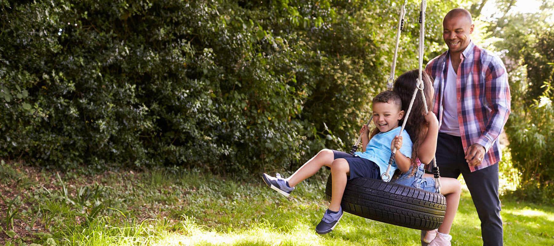 man pushing kids on tire swing