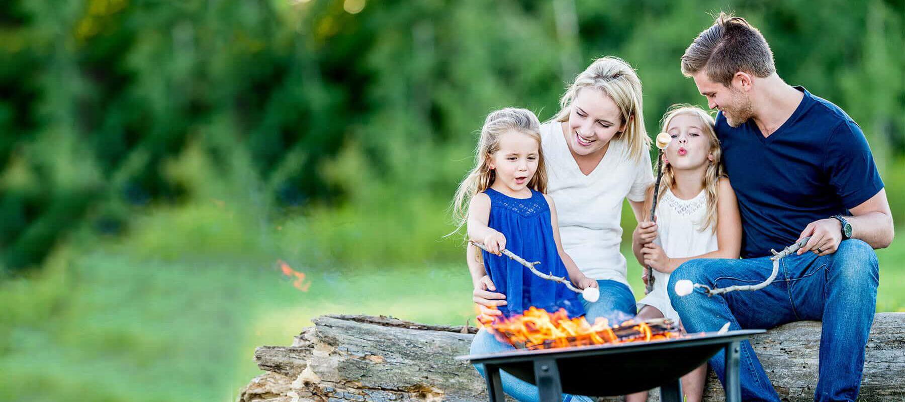 family sitting on log near fire pit