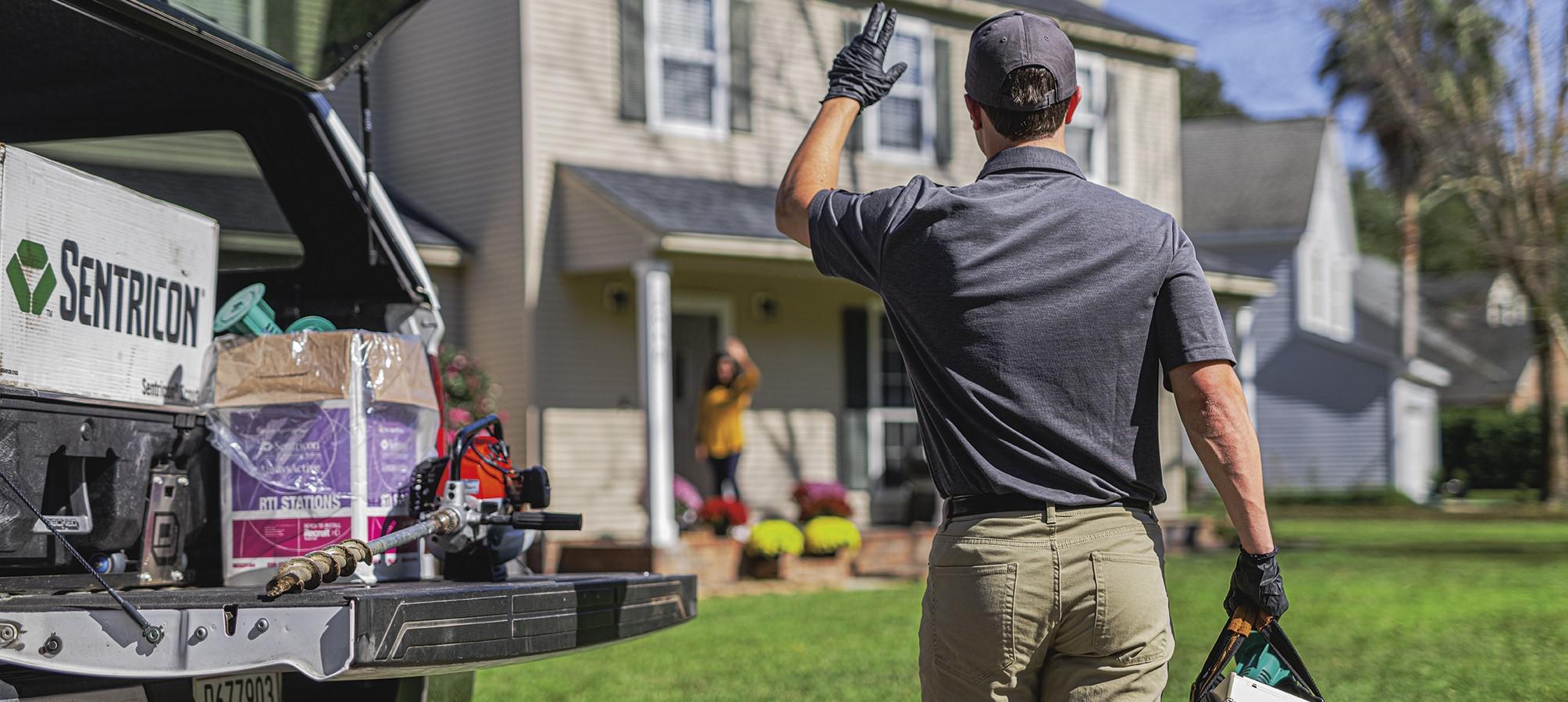 man with bag waving at women outside house